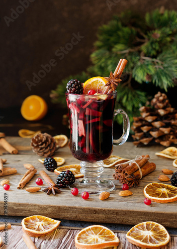 glass of hot mulled wine for the new year with ingredients for cooking, nuts and Christmas decorations