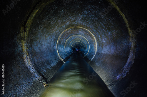 Dark underground sewer round concrete tunnel. Industrial wastewater and urban sewage flowing throw sewer pipe photo