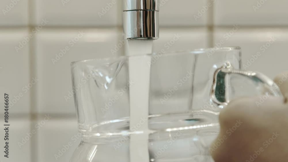 Man fills pitcher with clean water from tap in kitchen of house. Person puts transparent glass jug under metal faucet and stream of fresh pure aqua rushes into container. Drinking liquid fills big jar Man fills pitcher with clean water from tap in kitchen of house. Person puts transparent glass jug under metal faucet and stream of fresh pure aqua rushes into container. Drinking liquid fills big jar