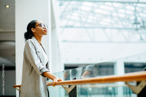 Print op canvas young african business woman in glasses dressed in gray suit holding on handrail when looking up and thinking indoor at modern business center