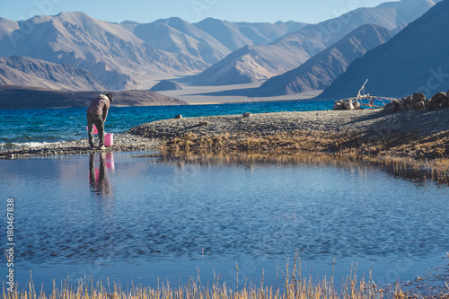 A man scooping up water in Pangong lake with mountains view and blue sky background