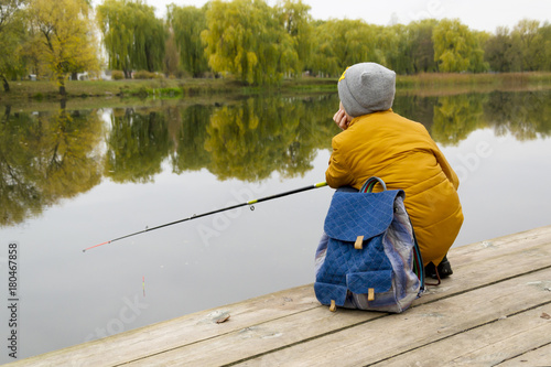 Side view on boy in yellow jacket using fishing rod outdoors at pond during cool autumn day