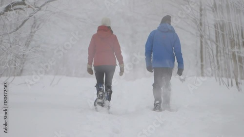 Two snowshoers walking side by side away from the camers on a previously taken path