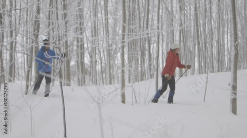 Two skiers are pushing there way across the ground while their side is facing the camera