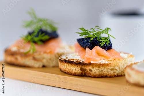 Appetizer toast bread with cream cheese, smoked salmon and black caviar decorated by dill.