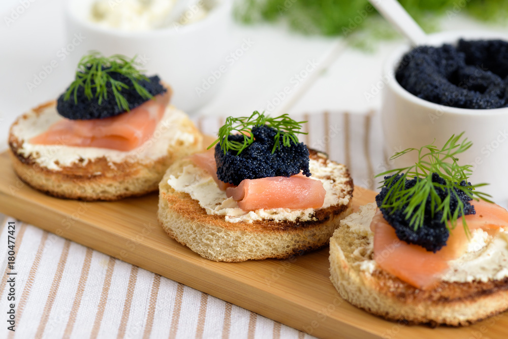 Appetizer toast bread with cream cheese, smoked salmon and black caviar decorated by dill.