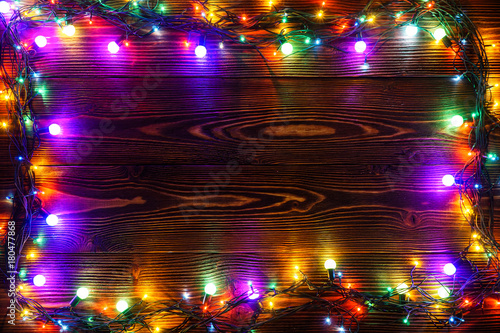 Wreath and garlands of colored light bulbs.Christmas background with lights and free text space. Christmas lights border. Glowing colorful Christmas lights on a wooden background. New Year.  