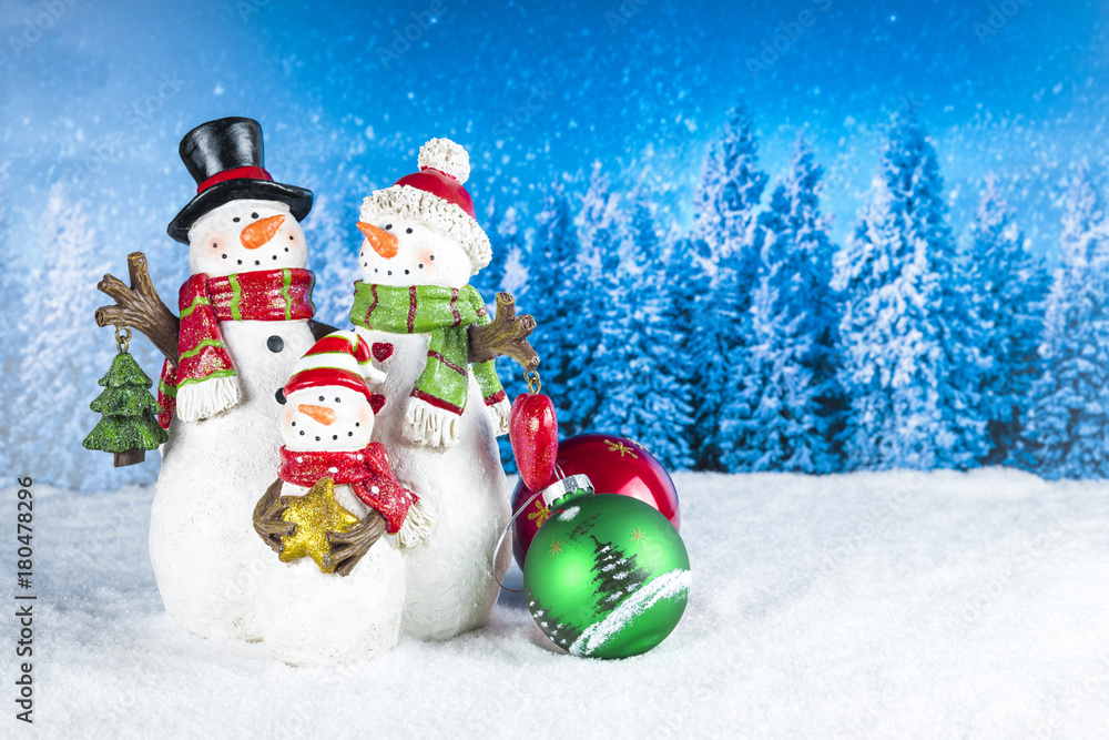Fototapeta premium Christmas decoration with snowman figurines as a family, red baubles on a blue snow pine tree landscape background