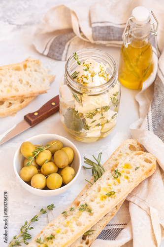 Green olives, feta cheese with olive oil in a jar and fresh ciabatta