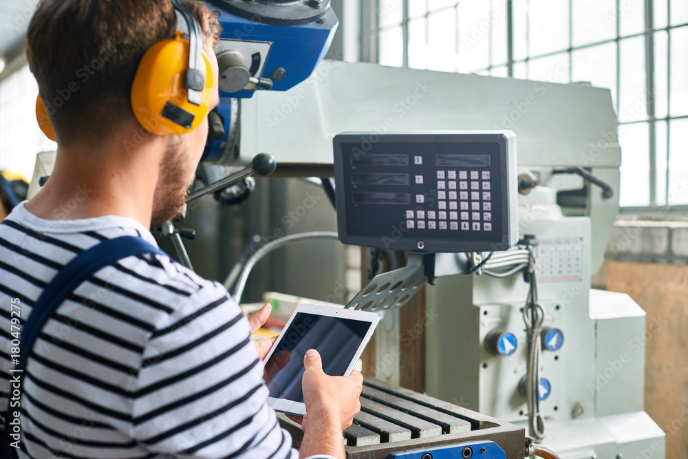 Back view portrait of young factory worker operating machine units at modern factory using digital tablet with electronic control, copy space Back view portrait of young factory worker operating machine units at modern factory using digital tablet with electronic control, copy space