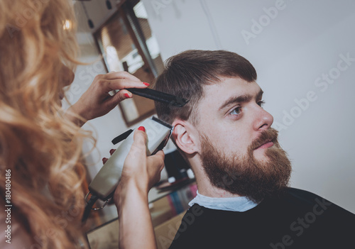 Master cuts hair and beard of men, hairdresser makes hairstyle for a young man. Hipsters