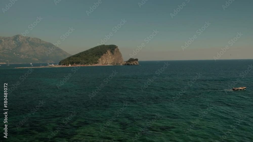 View of sea with boat on background of cliff and mountains on horizon. By blue waves private sea vessel travels along beautiful natural water area. View of sea with boat on background of cliff and mountains on horizon. By blue waves private sea vessel travels along beautiful natural water area.