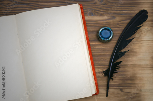 Open vintage book with blank paper page with copy space, black feather pen and inkwell on table background. Education background. Writer desk table. photo