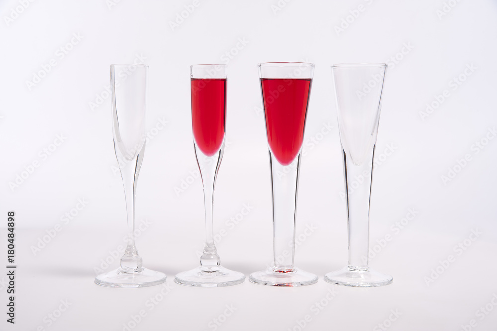 Glasses of red liqueur and empty glasses on white background