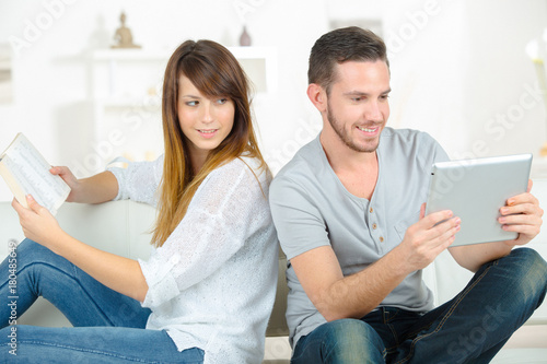 smiling young couple reading ebooks on sofa at home