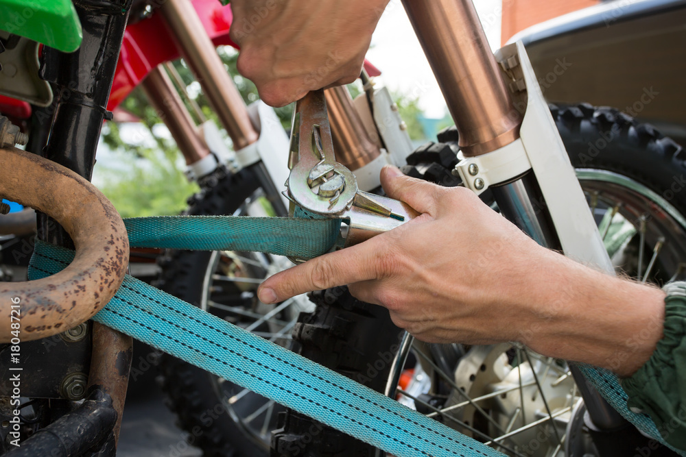 Man holding blue tie-down strap buckle that is used to secure motorcycle to a trailer or truck bed. Man holding blue tie-down strap buckle that is used to secure motorcycle to a trailer or truck bed.