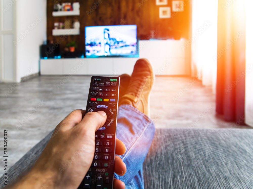Zappen / Fernsehen auf der Couch mit Fernbedienung in der Hand Stock