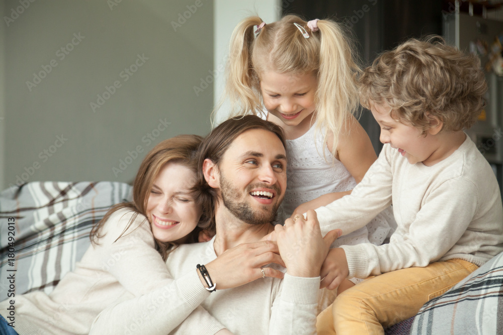 Cheerful parents and little children laughing having fun at home, wife with kids embracing hugging husband showing dad love, care and support, cozy loving family of four together, happy fathers day