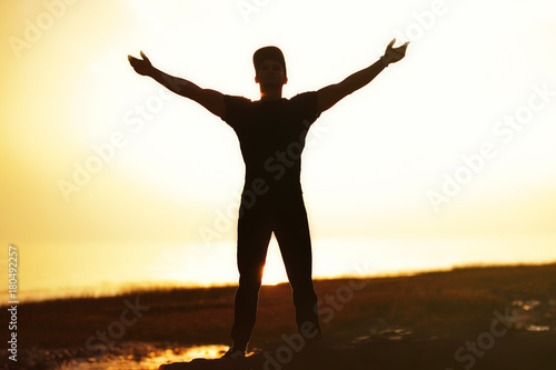 Silhouette of man with their hands raised in the sunset at the sea.