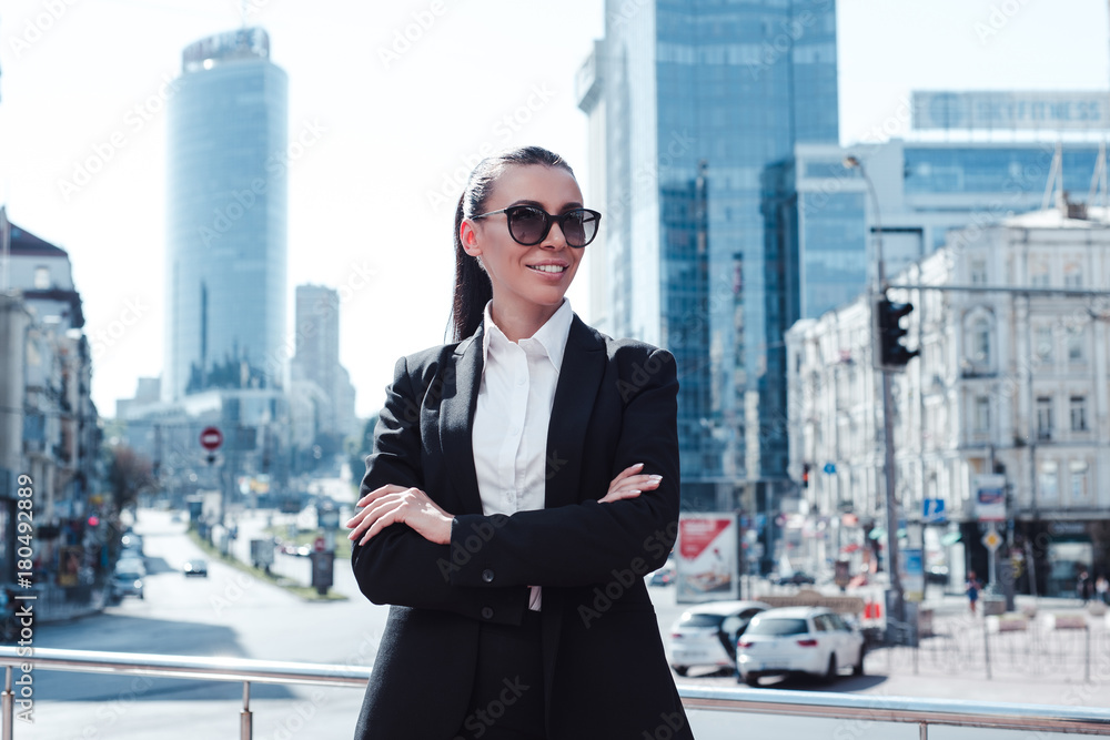 Confident at her business. Beautiful young businesswoman in sunglasses looking away with smile while standing outdoors Confident at her business. Beautiful young businesswoman in sunglasses looking away with smile while standing outdoors
