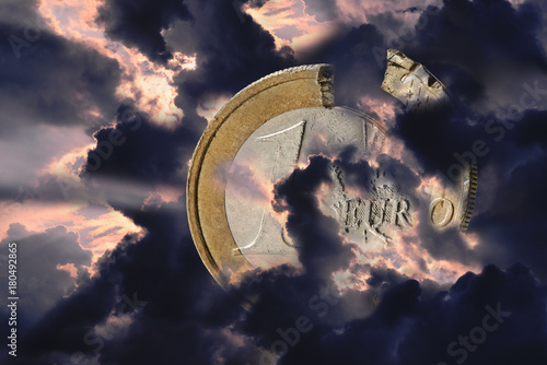 Eine beschädigte Euro Münze eingehüllt in unwetterwolken. Die wolken sind dunkel und glühen im hintergrund rot. Die europäische Union in der Kriese photo