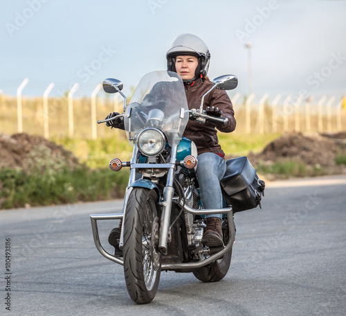 Fototapeta Naklejka Na Ścianę i Meble -  Woman motorcyclist riding solo on chopper on asphalt urban road