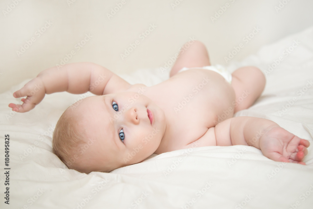 Beautiful smiling cute baby girl with blue eyes lying on the back on the bed in the room. Happy child laughing. Beautiful smiling cute baby girl with blue eyes lying on the back on the bed in the room. Happy child laughing.