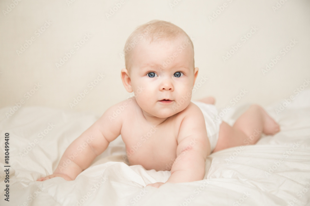 Beautiful smiling cute blonde baby girl with blue eyes lying  on the bed in the room. Happy child