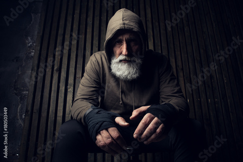 Serious bearded man ready to fight. Sport and fit man in hood sit on a chair. Workout and box sport. Extreme sport for old man. Close up portrait of man hands over his sports bandages