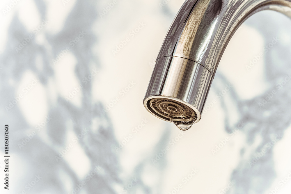 Chromed spout of a water tap with a drop on the aerator. Close-up. Chromed spout of a water tap with a drop on the aerator. Close-up.