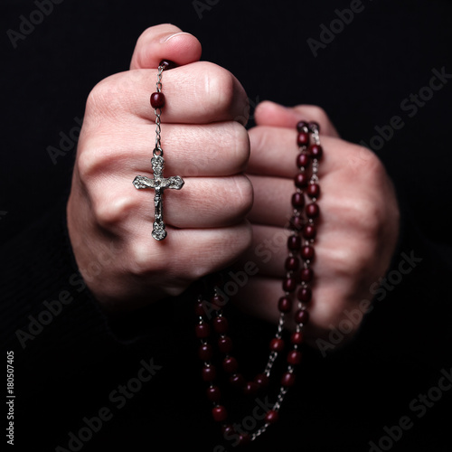 Female hands praying holding a rosary with Jesus Christ in the cross or Crucifix on black background. Woman with Christian Catholic religious faith