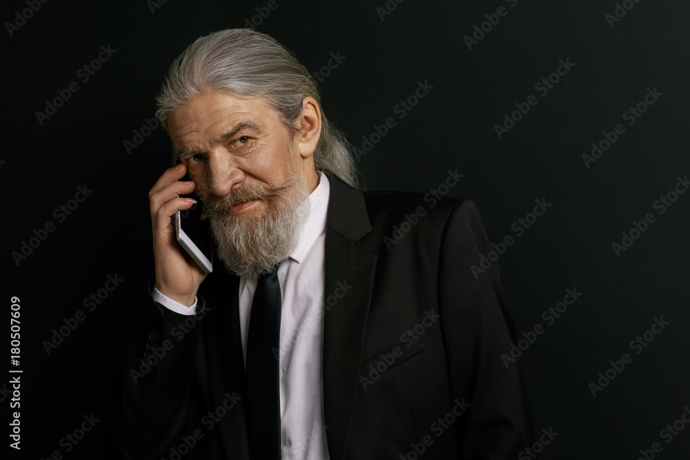 Stylish old male talking on cell phone. Elderly male in studio against black background holding mobile phone. Stylish old male talking on cell phone. Elderly male in studio against black background holding mobile phone.
