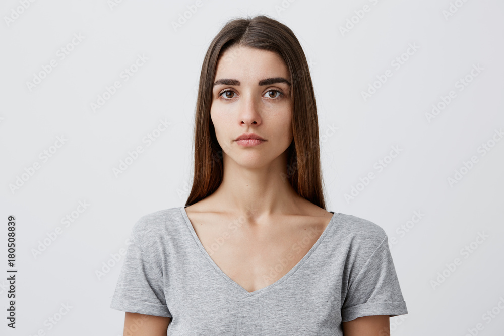 Close up of young handsome charming caucasian girl with long brown hair in gray t-shirt looking in camera with serious face expression. Woman getting photo for passport. Close up of young handsome charming caucasian girl with long brown hair in gray t-shirt looking in camera with serious face expression. Woman getting photo for passport.