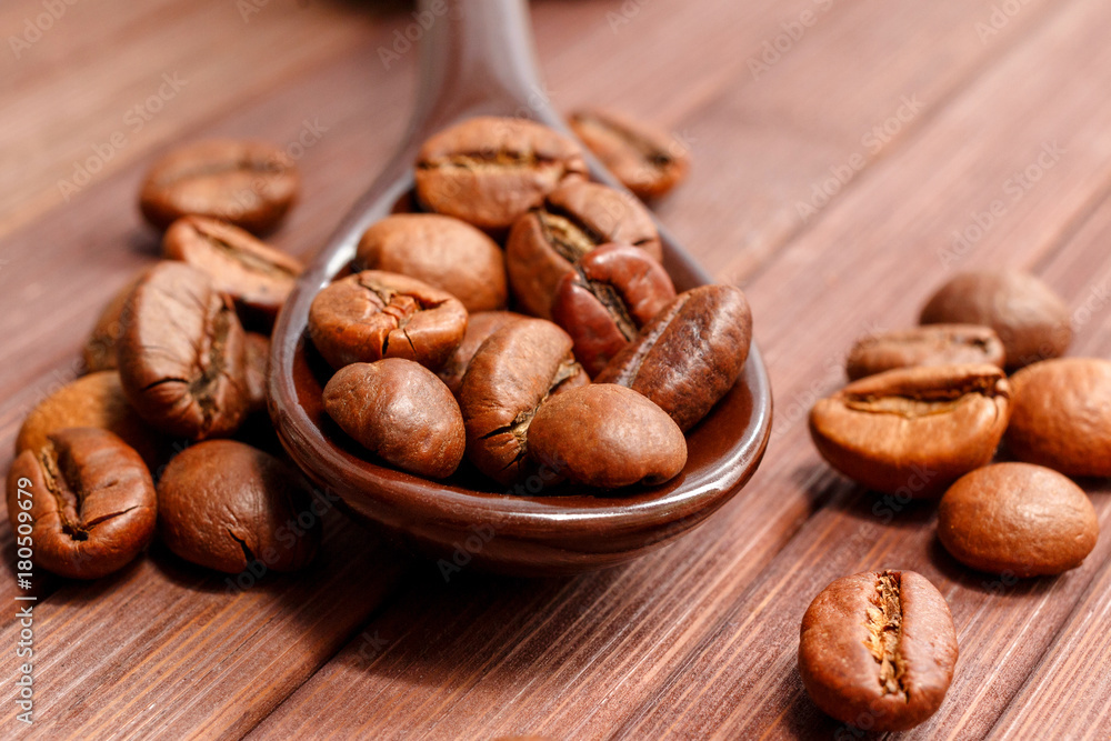 Grains of coffee close-up. Coffee beans are located on a spoon among the wooden texture. Coffee grains are located on a spoon on a wooden. Java composition from whole grains of coffee. Grains of coffee close-up. Coffee beans are located on a spoon among the wooden texture. Coffee grains are located on a spoon on a wooden. Java composition from whole grains of coffee.
