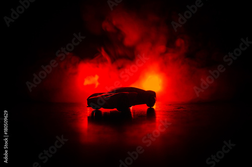 Fototapeta Naklejka Na Ścianę i Meble -  The car in the shadows with glowing lights in low light, or silhouette of sport car dark background