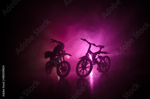 Silhouette of motorcycle and bicycle on a dark cloudy toned background. A silhouette of a motorcycle and bike from a side view. Selective focus