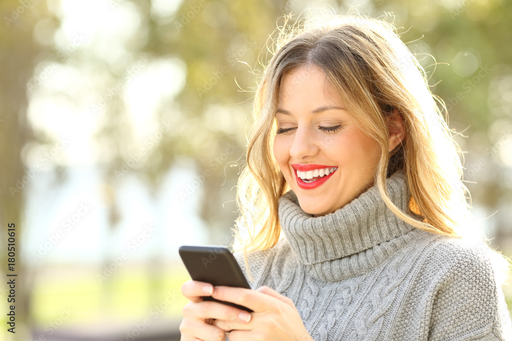 Happy woman reading text on phone in winter Happy woman reading text on phone in winter