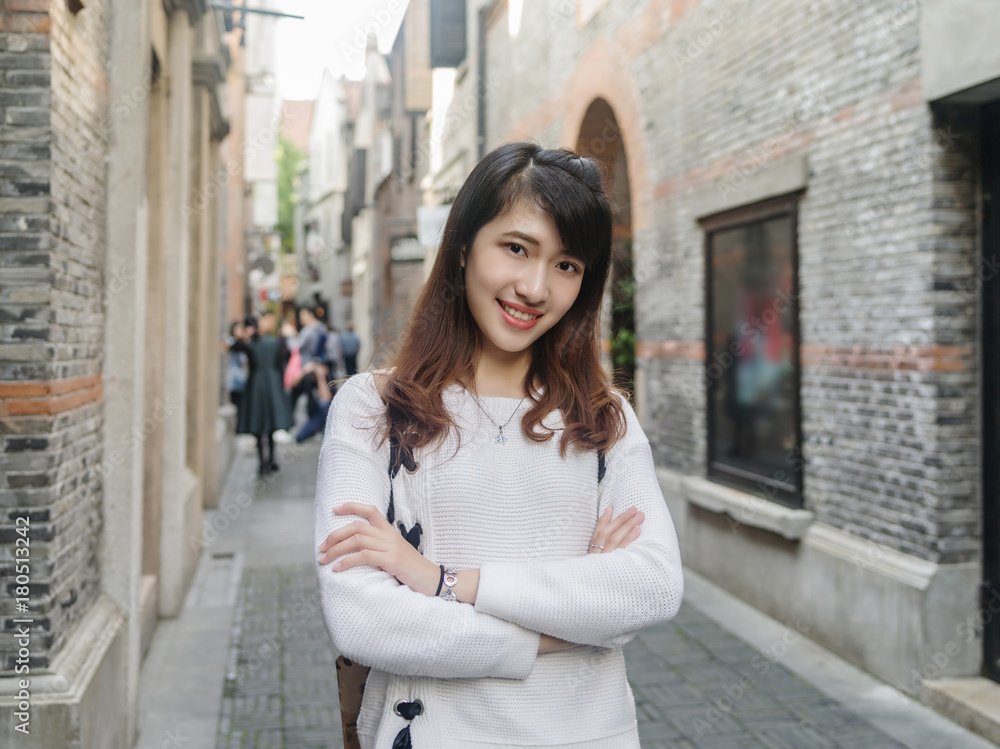 Portrait of beautiful young Chinese woman wearing white sweater and blue jeans in Shanghai Xintiandi, smiling with defocused Shikumen style street background,  Asian girl Concept ,Travel Concept.