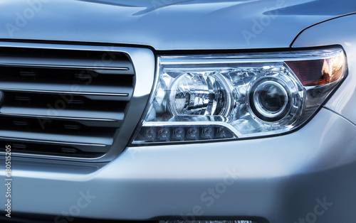 Blue toned close up photo of a car headlight with grille.