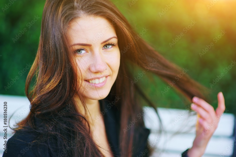 Portrait of beautiful girl with hair that flies in wind. Woman smiling with perfect smile and white teeth a park, looking at camera