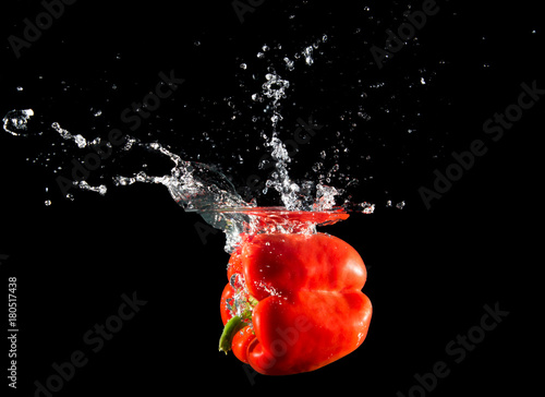 Bright red paprika falling in water on black background