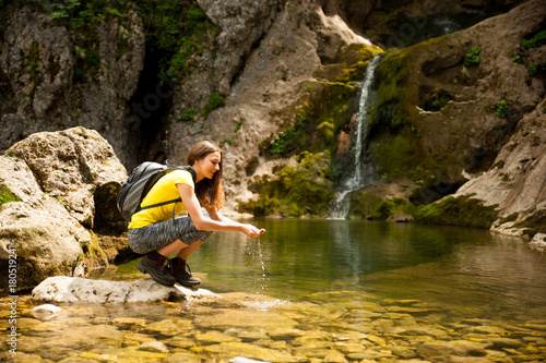 active young woman drinking water from a mountain creek on a warm spring day