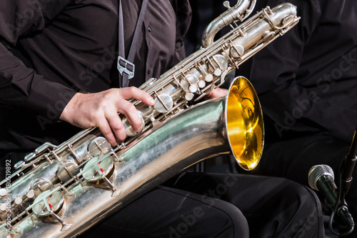Fotografie The baritone saxophone lies on the knee of the musician in a black shirt and trousers