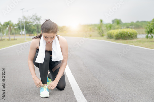 Portrait of young sports girl tying shoelaces on the road. © kwanchaichaiudom