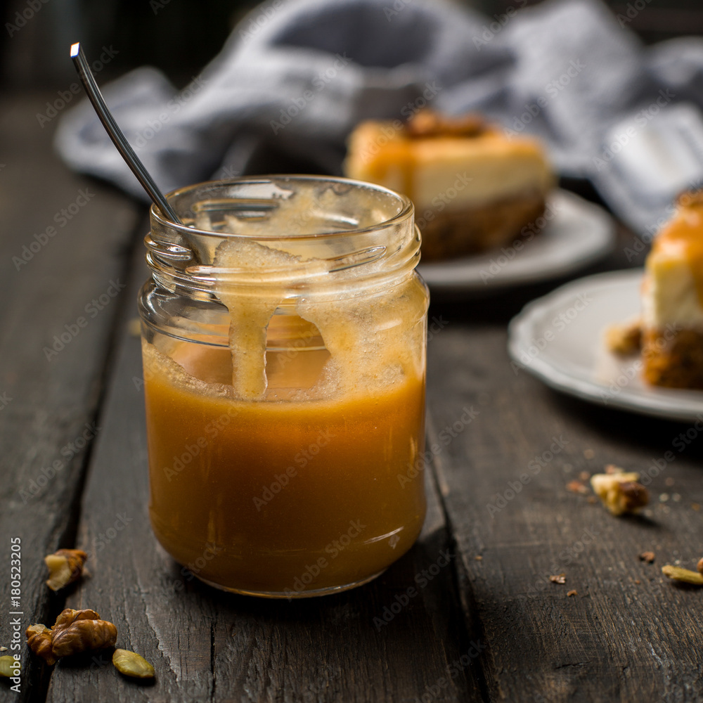 Caramel sauce in a jar. Carrot nut vanilla cheesecake with salty homemade caramel on a white plate on a dark wooden vintage background. Two pieces of homemade cheesecake. Caramel sauce in a jar. Carrot nut vanilla cheesecake with salty homemade caramel on a white plate on a dark wooden vintage background. Two pieces of homemade cheesecake.