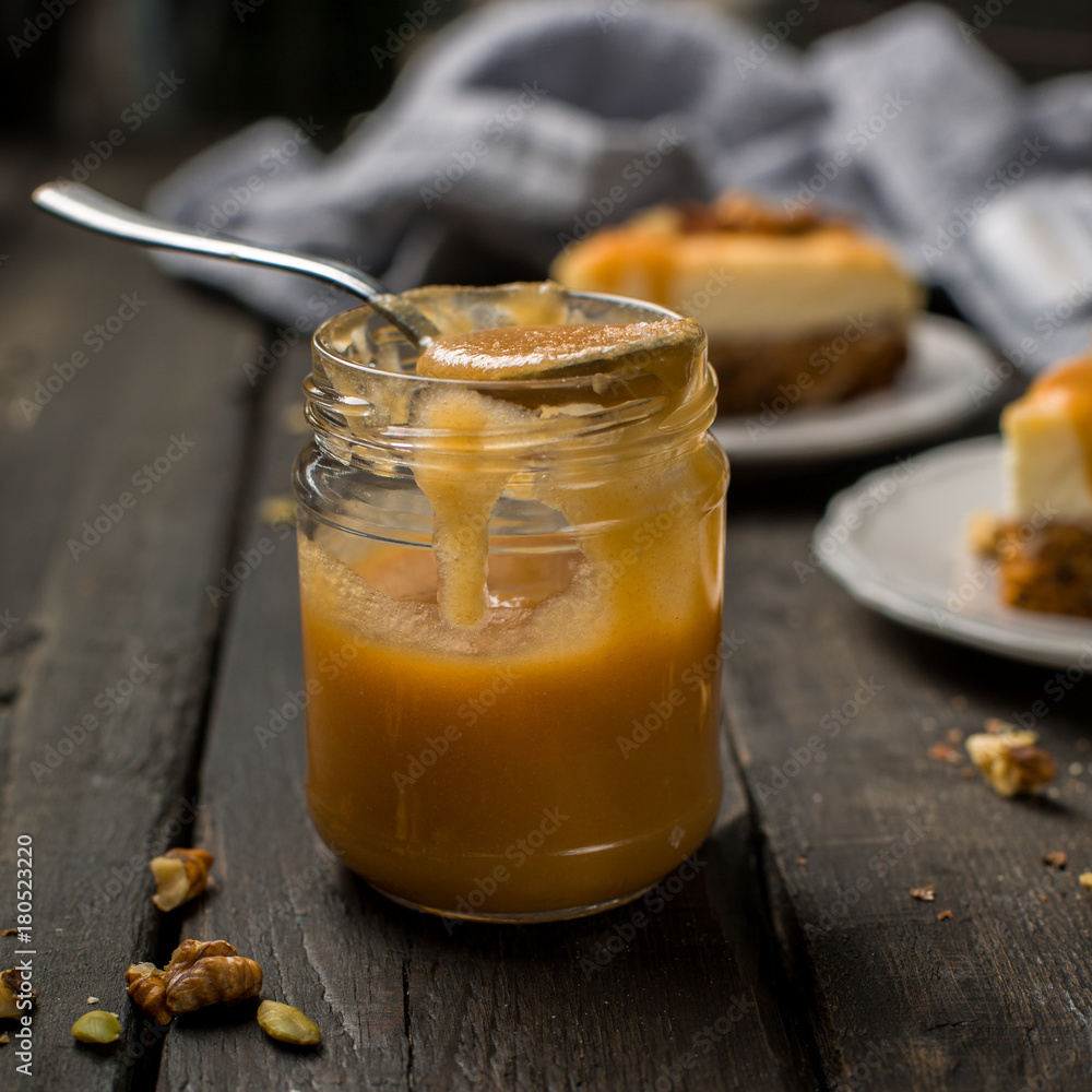 Caramel sauce in a jar. Carrot nut vanilla cheesecake with salty homemade caramel on a white plate on a dark wooden vintage background. Two pieces of homemade cheesecake. Caramel sauce in a jar. Carrot nut vanilla cheesecake with salty homemade caramel on a white plate on a dark wooden vintage background. Two pieces of homemade cheesecake.
