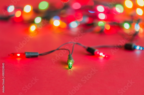 Xmas lights bulbs on string (selective focus) in blue, yellow, green, pink & red colours  on vivid red velvet background with copy space & bokeh (blur light) for Christmas tree, new year celebration © artissp