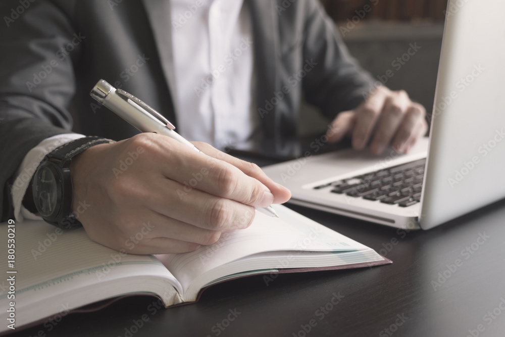 Close up of businessman writing note and using a laptop on the office desk. Close up of businessman writing note and using a laptop on the office desk.