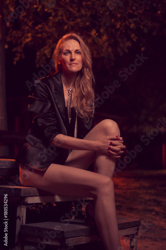 fashionable beautiful one mature Caucasian woman posing, late 40s, ex fashion model, posing portrait, sitting steps, outdoors orange red street lights
