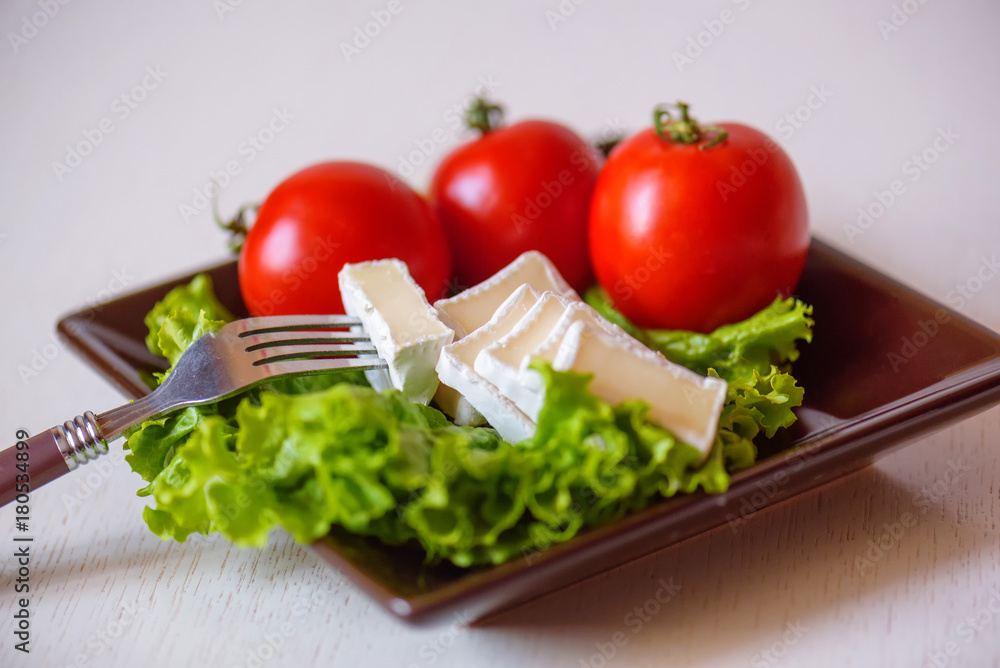 Tomatoes and cheese slices lie on a sheet of fresh salad in a plate.